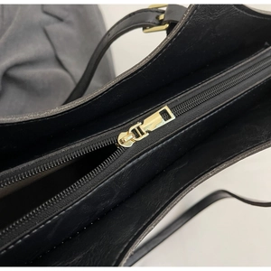Detailed close-up of smooth gold zipper closure on black faux leather tote bag
