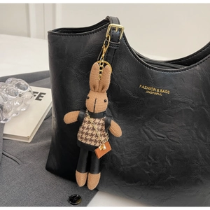 Detailed macro view of a brown knit rabbit charm hanging on a black leather tote bag