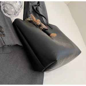 Detail of a large black leather tote bag with a cute bunny charm on a minimalist background