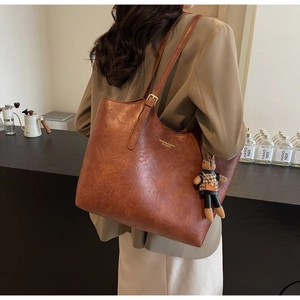 Detail of vintage brown tote bag in oil-wax texture with adjustable straps and plush charm