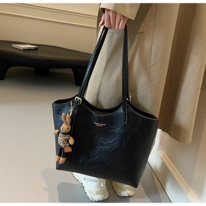 Detail of black faux leather tote bag with subtle wrinkled texture and rabbit charm