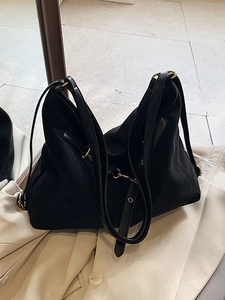 Matte black large capacity tote bag for women with golden hardware on a beige suit jacket