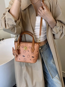 Orangefarbene Eimer-Tasche mit Bärenprint und Schleifenanhänger am Modell