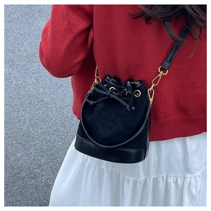 Détail du sac seau noir avec patchwork en daim et garnitures dorées porté par un mannequin