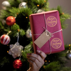 Detail of round gold foil Thank You sticker on red gift box with festive lights