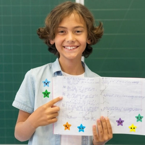 Child holding notebook with colorful star-shaped emoji reward stickers on green background