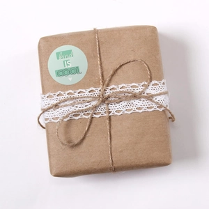Close-up of a 'kind IS COOL' round sticker on a gift box with lace and jute twine