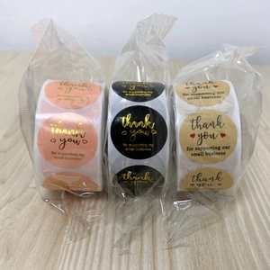 Three rolls of round thank you stickers in pink, black, and kraft for small business packaging