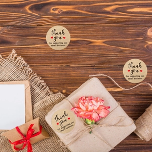 Detail of round kraft paper thank you sticker with red hearts on a rustic gift box