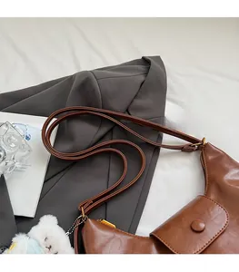 Détail du sac demi-lune en cuir marron avec poche à rabat et petit pendentif d'ours