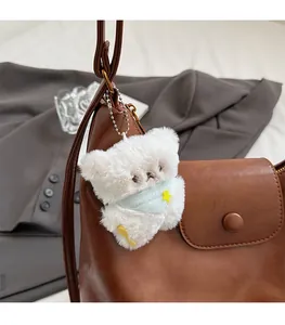 Porte-clés ours en peluche blanc avec écharpe bleue sur un sac cabas en cuir brun