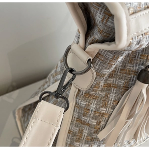 Detail der Tweed-Struktur mit goldener Metallschnalle und weißer Quaste an der Handtasche