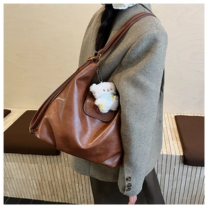 Détail d'un grand sac cabas en cuir marron souple avec un petit pendentif ours en peluche blanc