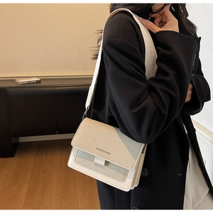 Dettaglio della patta beige testurizzata e della tracolla in tessuto di una borsa a tracolla
