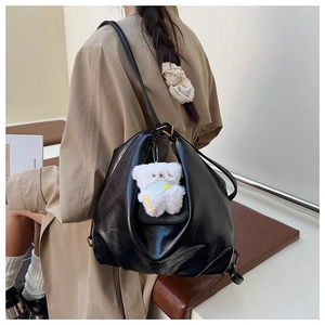 Détail du sac hobo en cuir brillant noir avec design plissé et breloque ours mignon