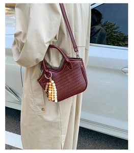 Détail du sac seau tressé rouge foncé avec pompon en perles colorées et bandoulière