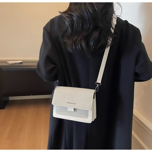 Dettaglio borsa a tracolla crema con testo Fashion & Bags su un blazer nero