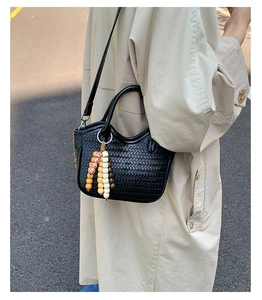 Close-up of black woven bucket bag with beaded charm and slim leather strap detail