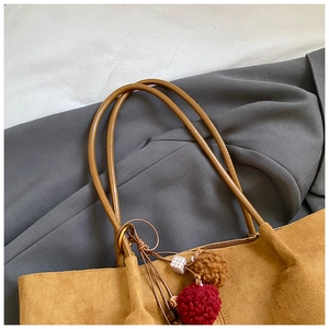 Detail of caramel suede tote bag with plush pompom charms and slender shoulder straps