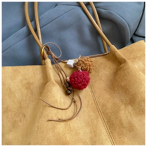 Detail of vintage suede tote bag with colorful pom-pom charms on grey fabric background