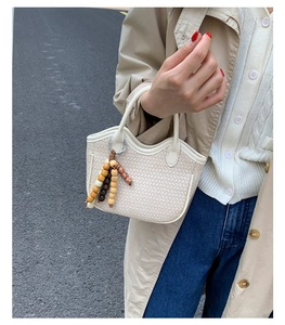 Detail of a beige woven bucket bag featuring decorative wooden bead tassels and dual handles