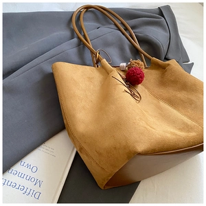 Detail of suede tote bag texture with plush ball charm on casual grey coat backdrop
