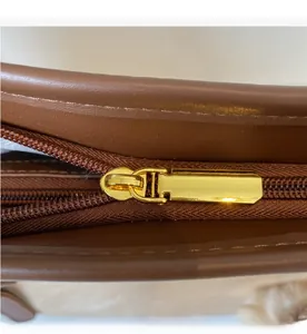 Detail of a smooth gold metal zipper on a premium brown leather tote bag with a macro view