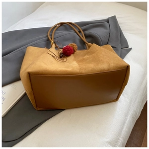 Close-up of camel suede tote bag with plush pompom charms on a stylish grey blazer