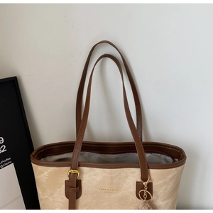 Detail of beige canvas tote bag with brown leather handles and brand logo engraving