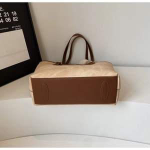 Close-up of contrast stitching on beige canvas tote bag with reinforced brown leather base