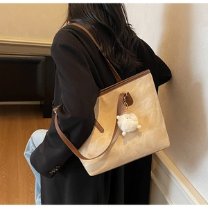 Close-up of beige tote bag with brown leather straps and a plush bear pendant on model