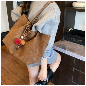Detailed view of brown matte tote bag with fuzzy pom-pom charms and tassel on model