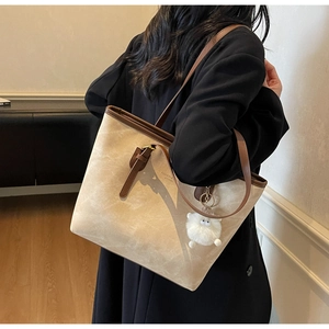 Detail of beige tote bag with brown trim and plush monster charm worn by a model
