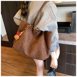 Detailed view of brown faux suede tote bag with decorative pom-pom tassel and dual straps