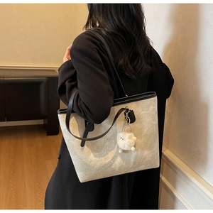 Detail view of contrast large tote bag with black straps and plush sheep charm on shoulder