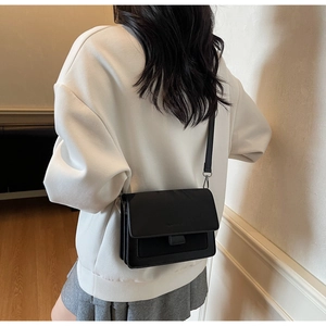 Dettaglio di una borsa a tracolla minimalista in pelle nera con tracolla larga sul modello