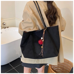 Detail of black suede tote bag featuring a red pompom and leather tassel charm accessory