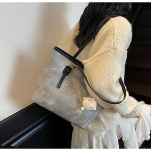 Detail view of grey textured tote bag with black straps and a cute white plush pendant