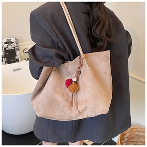 Close-up of khaki suede tote bag with decorative pompom charm on a shoulder strap