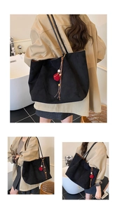 Detail of black large tote bag featuring red pompom charm and leather fringe tassel