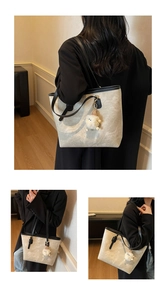 Detail of grey textured tote bag with black leather straps and plush charm accessory