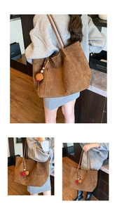 Detail of a large brown suede tote bag featuring slim leather straps and a colorful pompom charm