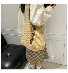 Detail view of striped beige knit tote bag with boho beads shown on a model's shoulder