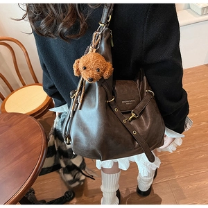 Detail of dark brown leather tote bag featuring a plush dog charm and adjustable strap