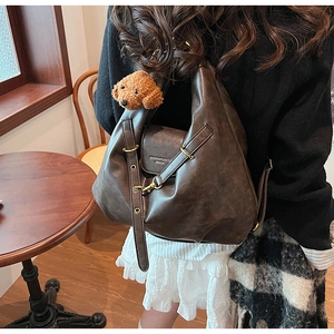 Detail of dark brown faux leather tote bag with gold logo and plush dog charm