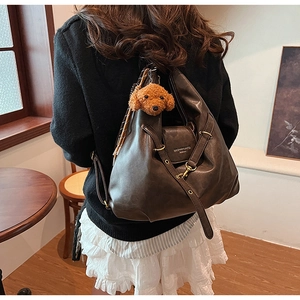 Detail of dark brown leather tote bag with plush dog charm and branded lettering