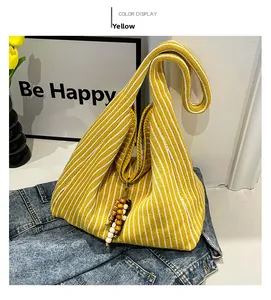 Detail of yellow and white striped knit tote bag with wooden bead charm on denim jeans