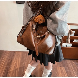 Detail of a brown leather tote with a teddy bear charm and braided strap detail