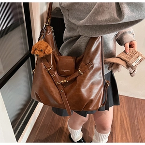 Brown leather tote bag featuring adjustable shoulder strap and cute plush bear accessory