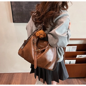 Brown leather tote bag featuring a cute plush dog pendant and adjustable shoulder strap